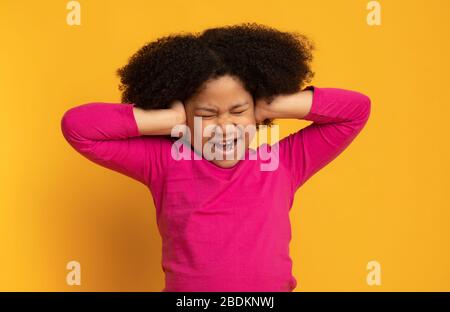 Portrait de la petite fille africaine agacée couvrant les oreilles avec les mains Banque D'Images