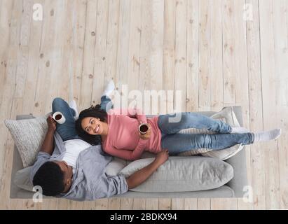 Isolement à la maison. Couple noir souriant reposant avec café, vue sur le dessus Banque D'Images