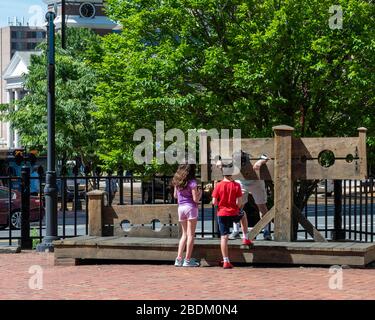 Deux enfants, un garçon et une fille qui se tiennent devant un homme dans les stocks dans la cour de la maison d'État ancienne, au centre-ville de Hartford CT Banque D'Images