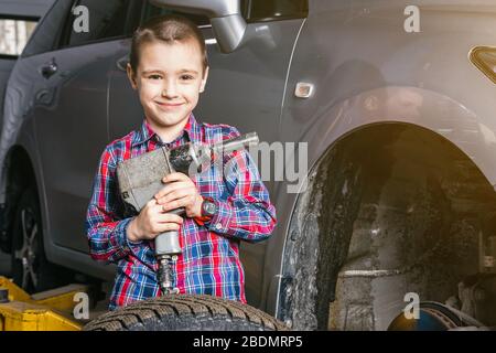 Un jeune garçon, un jeune travailleur automobile, fait un changement de pneu avec une clé pneumatique dans le garage d'une station de service. Un enfant apprend la changine mécanique Banque D'Images