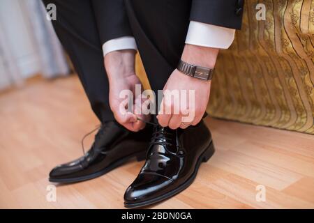 Vue rapprochée des mains des hommes laçage de belles chaussures élégantes. Jour de mariage. Groom attacher sa chaussure . Homme portant un costume mettant ses chaussures brunes sur. Mains et Banque D'Images