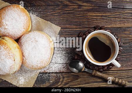 Beignets sucrés saupoudrés de sucre en poudre et tasse à café sur table en bois, vue sur le dessus Banque D'Images