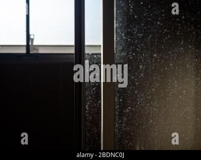 Porte en verre sale et poussiéreuse. Tache d'eau sur la porte coulissante dans la salle de bains, fond sombre. Banque D'Images