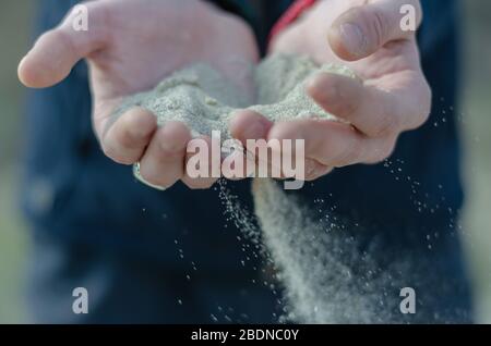 Le sable coule à travers mes doigts. Le vent souffle les grains de sable blanc. Les flocons de sable s'écoulent d'une poignée de jeunes hommes. Mise au point sélective. Gros plan. Banque D'Images