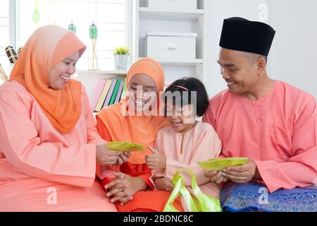 Femme donnant un paquet vert aux filles pendant hari raya. Malais ou famille malaisienne à la maison. Banque D'Images