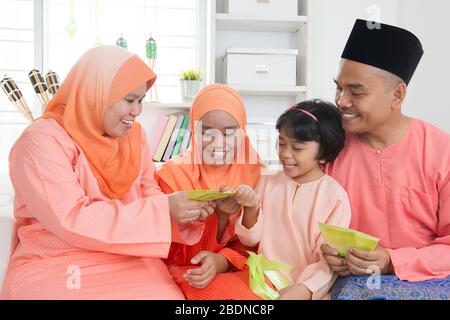 Femme donnant un paquet vert aux filles pendant hari raya. Malais ou famille malaisienne à la maison. Banque D'Images