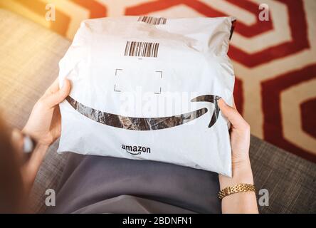 Paris, France - 1 août 2019 : vue aérienne d'une femme élégante sur le salon canapé tenant un colis en plastique Amazon Prime frais avec le sourire emblématique du logotype Banque D'Images