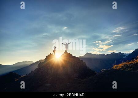 Deux randonneurs en silhouette se dresse sur la roche dans les belles montagnes avec des mains au lever du soleil, le fond de ciel Banque D'Images