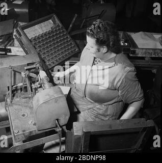 Années 1950, historique, une travailleuse sur le plancher de l'atelier portant des combinaisons assis à la machinerie et à côté d'un plateau de bobbin en bois dans une usine industrielle de fabrication de piles zinc-carbone, Londres, Angleterre. En Grande-Bretagne d'après-guerre, beaucoup de femmes qui sont allées dans les usines pour aider l'effort de guerre y sont restées après la guerre, car elles ont gagné de l'argent pour soutenir leurs familles. Banque D'Images