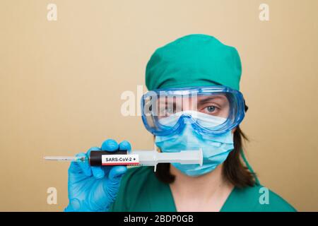 Le médecin féminin en costume vert et les gants bleus contiennent une seringue avec du sang positif COVID-19 sur le fond jaune. Concept médical. Mise au point sélective. Banque D'Images