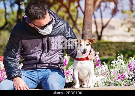 Homme portant un masque de visage regardant le chien pendant le coronavirus. De courtes promenades pendant la pandémie de covid-19. Évitez tout contact avec votre animal pendant le covid-19 Banque D'Images
