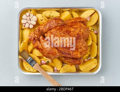 poulet mariné entier en sauce avec pommes de terre crues, avec brosse dans un plat de cuisson, vue du dessus. Banque D'Images