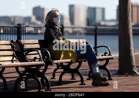 Femme portant un masque lorsqu'elle est assise sur un banc à Piers Park, Boston, Massachusetts, États-Unis Banque D'Images