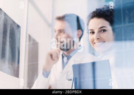 Les médecins professionnels qui examinent les rayons X d'un patient et discutent, un jeune praticien souriait à l'appareil photo Banque D'Images