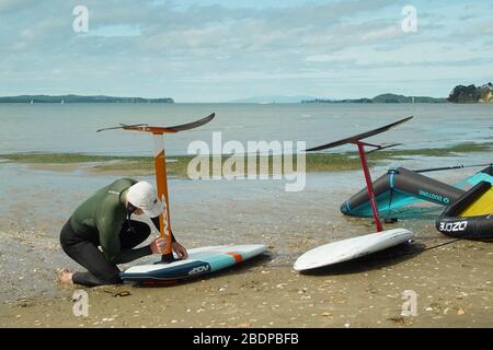 Deux hommes préparent leur équipement pour faire du carrelage dans les ailes à l'aide d'ailes gonflables et de planches de surf hydrofoil à Auckland Harbour. Banque D'Images