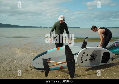 Deux hommes préparent leur équipement pour faire du carrelage dans les ailes à l'aide d'ailes gonflables et de planches de surf hydrofoil à Auckland Harbour. Banque D'Images