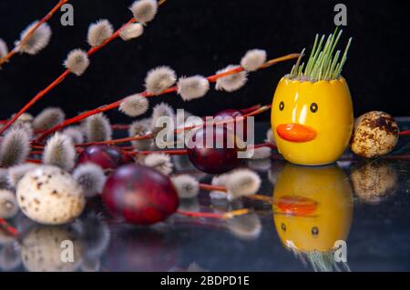 Branches de saule, œufs peints et canard en céramique avec du blé dépoli sur un comptoir en verre foncé. Banque D'Images