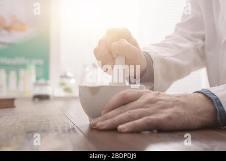 Pharmacien professionnel meuler une préparation médicale à l'aide d'un mortier et d'un pilon, d'une pharmacie et d'un concept de médecine, les mains se rapprochés Banque D'Images