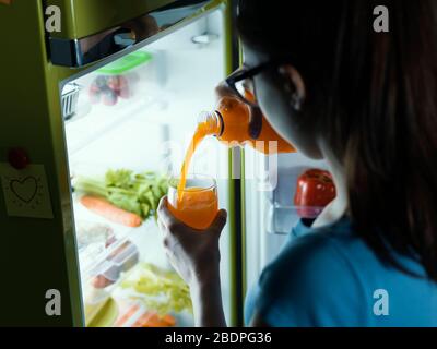 Femme prenant une bouteille de jus d'orange frais du réfrigérateur et la verser dans un verre, un concept de boisson saine Banque D'Images