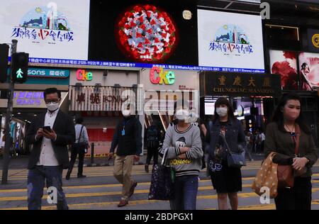 Hong Kong, CHINE. 9 avril 2020. Les citoyens masqués traversent le zébra traversant un grand écran derrière projeter une image microscopique du CORONAVIRUS. Avril-9, 2020 Hong Kong.ZUMA/Liau Chung-ren crédit: Liau Chung-ren/ZUMA Wire/Alay Live News Banque D'Images