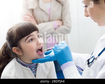 Médecin professionnel vérifiant la gorge d'une fille, elle ouvre la bouche Banque D'Images