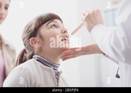 Médecin professionnel vérifiant la gorge d'une fille, elle ouvre la bouche Banque D'Images