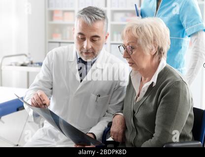 Radiologue professionnel examinant une image radiographique avec un patient senior lors d'une visite à la clinique, le médecin pointe et donne des conseils Banque D'Images