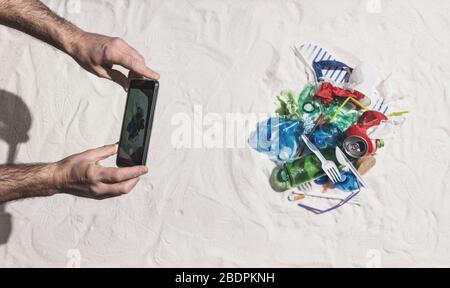 Homme prenant une photo de la pollution des déchets sur la plage et la partager en ligne à l'aide de son smartphone, protection de l'environnement et pollution plastique conceps Banque D'Images