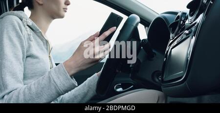 La jeune femme méprise et négligente utilise son smartphone pendant la conduite, en conduisant le concept de sécurité Banque D'Images