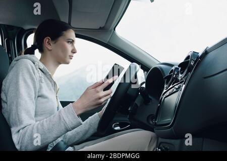 La jeune femme méprise et négligente utilise son smartphone pendant la conduite, en conduisant le concept de sécurité Banque D'Images