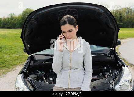 Jeune femme triste appelant un service de réparation de voiture avec son téléphone, elle a une panne de voiture dans une route de campagne Banque D'Images