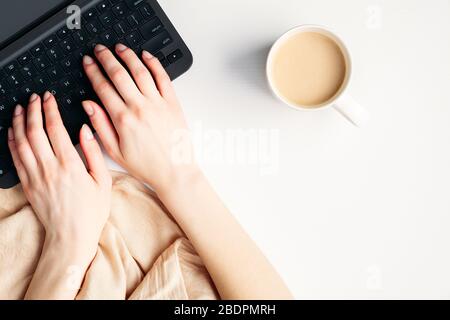 Mains féminines en tapant un texte sur la vue supérieure du clavier de l'ordinateur portable. Espace de travail moderne minimaliste féminin avec couverture, tasse à café et carnet Banque D'Images