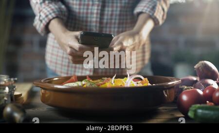 Femme préparant un repas sain avec des légumes frais et prenant une photo avec son smartphone Banque D'Images