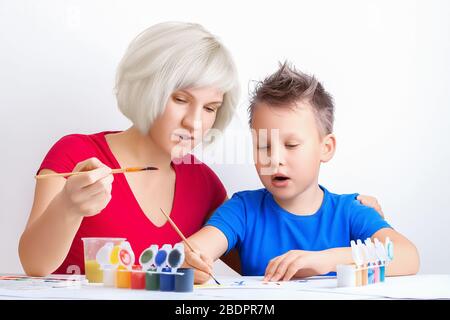 Jolie jeune fille enseigne à dessiner un joli garçon. Maman et fils peignent ensemble. Éducation, leçons personnelles, loisirs, activités familiales pendant la quarantaine Banque D'Images