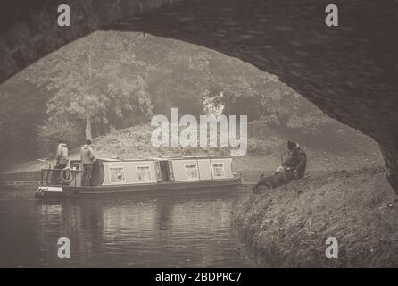 Vue à l'ancienne, en noir et blanc sur les pêcheurs assis sur la rive britannique du canal, pêcher dans l'eau du canal avec le bateau à narrowboat qui passe. Tranquillité. Banque D'Images