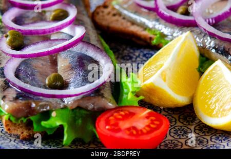 Le smorrebrod appétissant avec le hareng norvégien, la laitue, l'oignon bleu, le citron et la tomate se trouve sur une planche en bois Banque D'Images