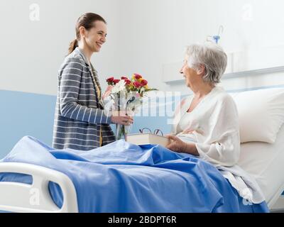 Jeune femme visitant sa grand-mère à l'hôpital et donnant ses fleurs Banque D'Images