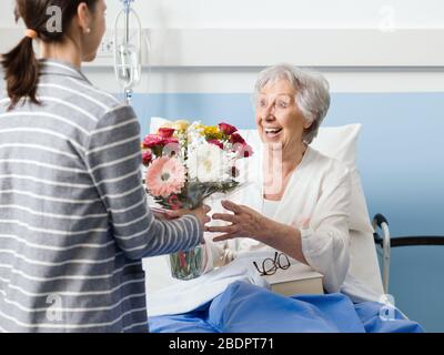 Jeune femme visitant sa grand-mère à l'hôpital et donnant ses fleurs Banque D'Images