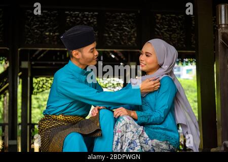 Un portrait de jeune couple de malay musulman en costume traditionnel montrant un geste romantique pendant la célébration de l'Aidilfitri. Homme ajustant sa petite amie Banque D'Images