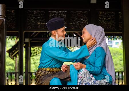 Un portrait de jeune couple de malay musulman en costume traditionnel montrant un geste romantique pendant la célébration de l'Aidilfitri. Homme ajustant sa petite amie Banque D'Images