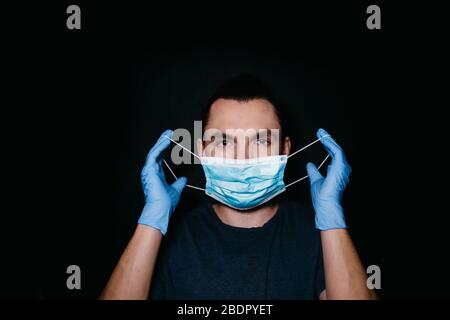 Concept de prévention COVID-19. Un jeune homme de race blanche met un masque médical sur fond noir. Portrait d'un homme regardant l'appareil photo dans un Banque D'Images