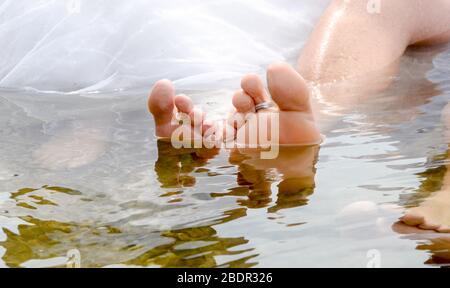 Anneaux placés sur les pieds submergés dans l'eau des jeunes mariés. Banque D'Images