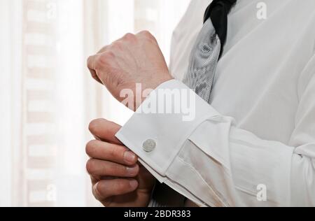 Boutons de manchette argentés qu'un homme met sur le poignet de sa chemise blanche. Banque D'Images