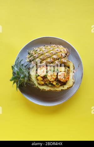 Vue sur les yeux d'oiseaux riz frit à base de ananas avec crevettes dans l'ananas sur une plaque blanche avec fond jaune, contenant de nourriture écologique Banque D'Images