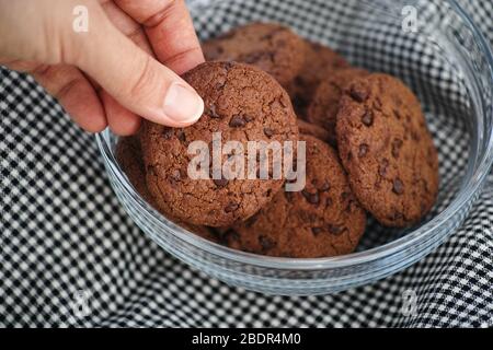 Une personne prenant un cookie maison au chocolat cuit à la carte dans un bol en verre. Gros plan. Banque D'Images