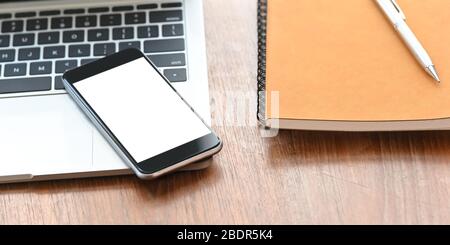 Gros plan smartphone avec écran blanc vide mettant sur le clavier d'ordinateur portable qui flot sur le bureau en bois avec ordinateur portable et stylo. Bureau equi Banque D'Images