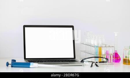 Photo de l'équipement d'expériences scientifiques mettant sur un bureau blanc de travail avec un ordinateur portable blanc à écran vide. Ordinateur portable plat, chimie g Banque D'Images