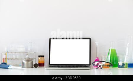 Photo de l'équipement d'expériences scientifiques mettant sur un bureau blanc de travail avec un ordinateur portable blanc à écran vide. Ordinateur portable plat, chimie g Banque D'Images