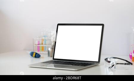 Photo de l'équipement d'expériences scientifiques mettant sur un bureau blanc de travail avec un ordinateur portable blanc à écran vide. Ordinateur portable plat, chimie g Banque D'Images