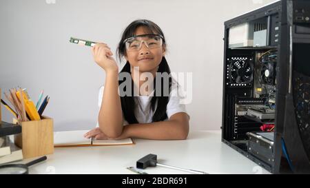 Photo de adorable fille d'école apprenant à fixer un matériel informatique qui met sur le bureau de travail blanc avec un tournevis et l'équipement de technicien sur wh Banque D'Images